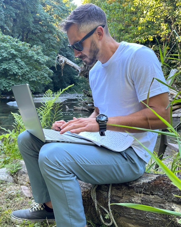 Patrick working on a laptop on a river bank, handwritten notes beside him